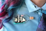 Woman with pink and blue hair wears ship in a bottle brooch to depict how to wear brooches for personal style.