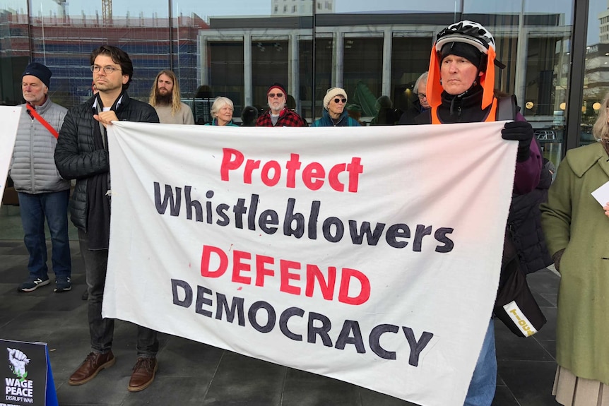 Protesters hold a banner reading "protect whistleblowers defend democracy".