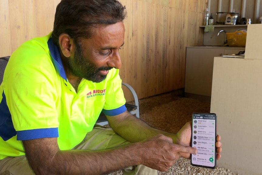 Mintu in a fluoro yellow work shirt sits holding a smart phone that displays comments on one of his YouTube videos. 