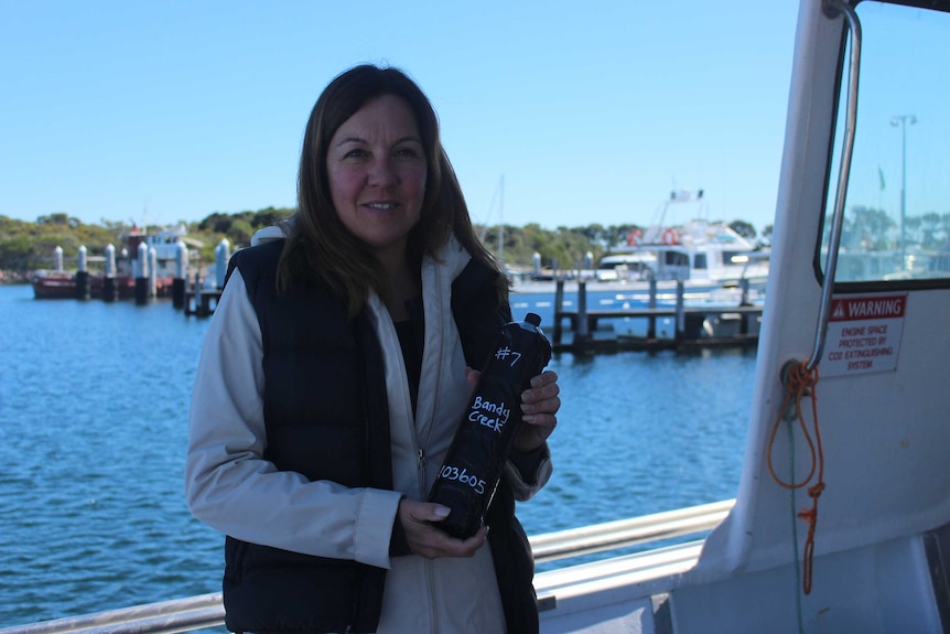 A woman stands on a boat holding a small canister wrapped in tape