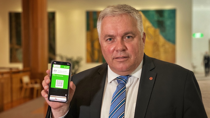 A man in a suit holds up his phone, with an apparent government website visible on the screen