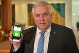 A man in a suit holds up his phone, with an apparent government website visible on the screen