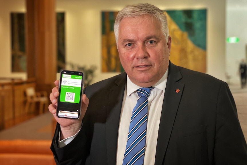 A man in a suit holds up his phone, with an apparent government website visible on the screen