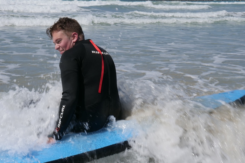 year 11 school boy in shallow waves on surf board about to topple over