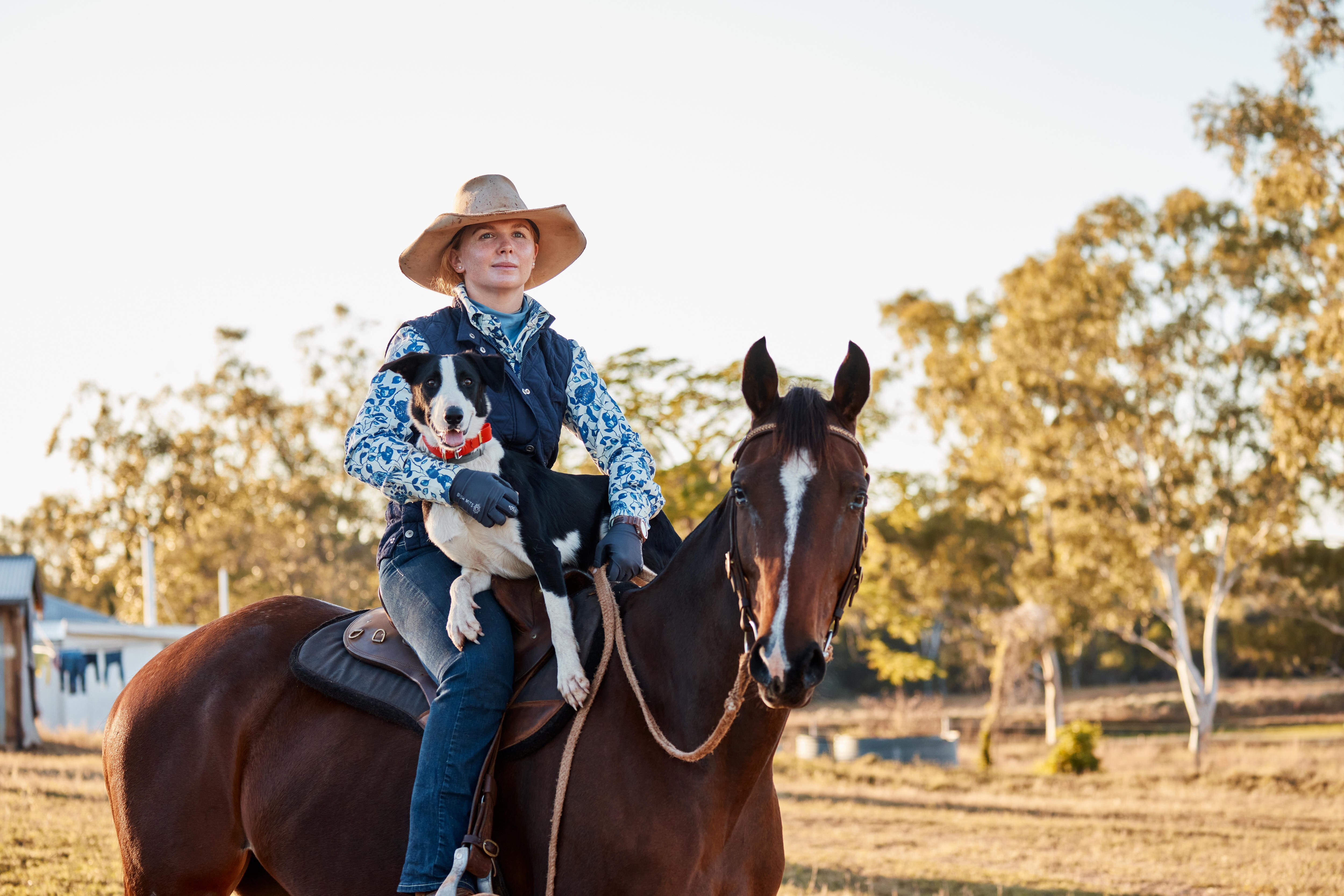 A woman sits on a horse, a dog on her lap.