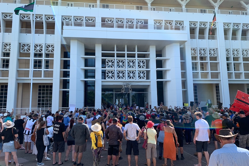A large group of people are protesting outside the Northern Territory Parliament House building.