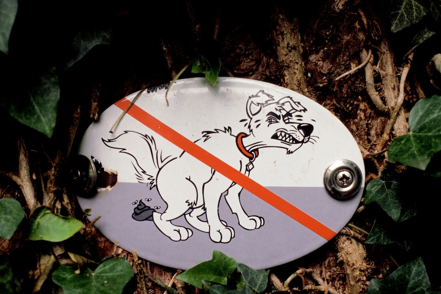 A sign of a cartoon dog defecating, with a red cross across it.