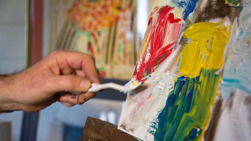 A paint covered brush spreads paint across a canvas.