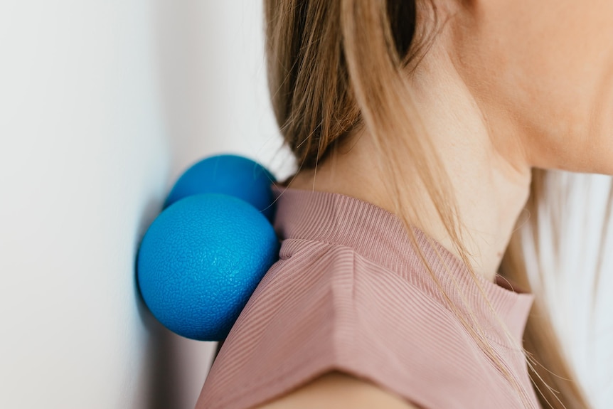 A woman leans against a wall with a blue foam cylinder behind her neck
