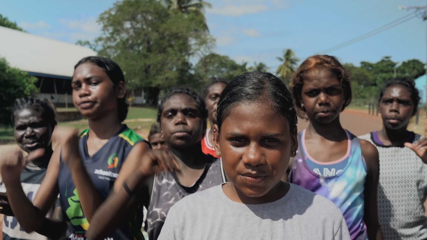 A group of young Indigenous women walk down the street towards the camera, the lead girl is smiling