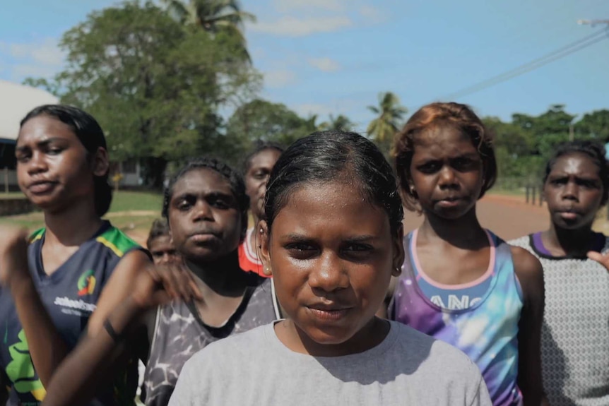 A group of young Indigenous women walk down the street towards the camera, the lead girl is smiling