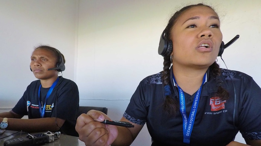 Two women sit at a desk in the commentary box with headphones on
