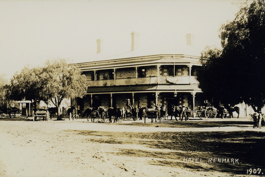 An old black and white photo of a historic hotel building with horses out the front. 