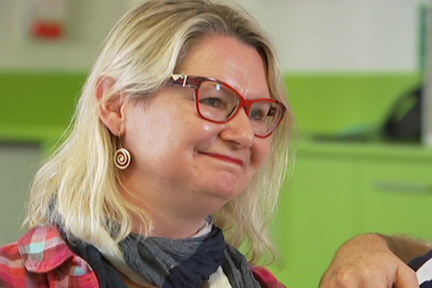A woman with collar-length blonde hair and wearing red glasses