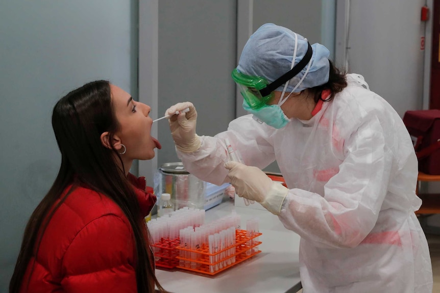 A female health worker in hazmat gear takes a swab from a woman's throat