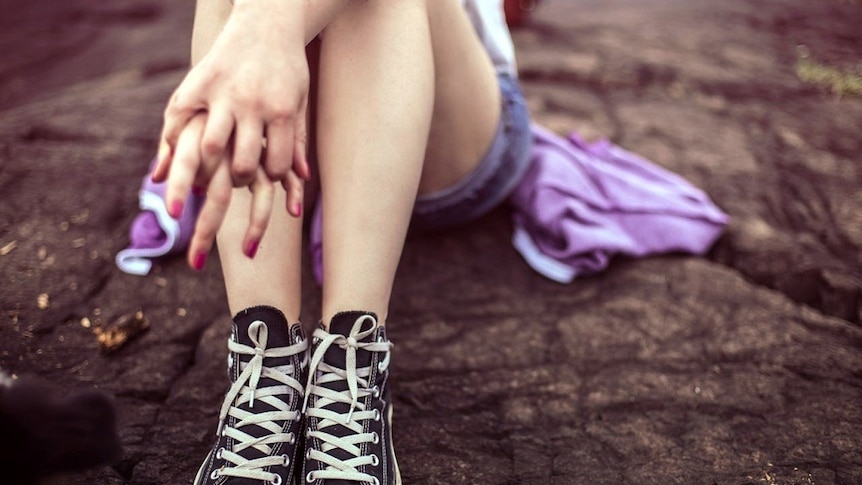 Girl sitting down with her hands clasped.