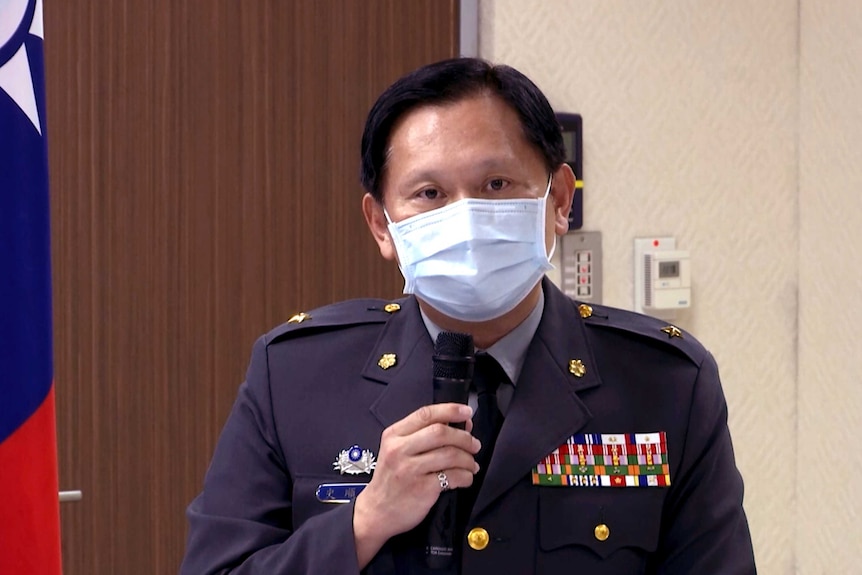 A Taiwanese official wearing a mask and decorated jacket holds a microphone.