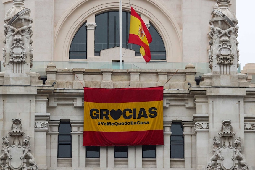 Two Spanish flags hang on a building, one with 'gracias' written on it.