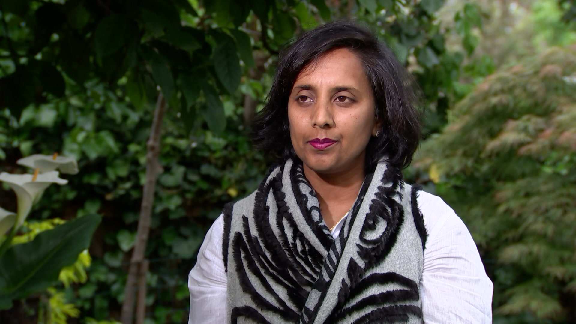 Michelle Ananda-Rajah stands outside, in front of greenery.