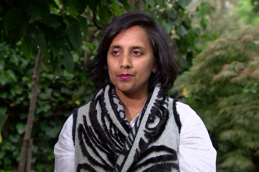 Michelle Ananda-Rajah stands outside, in front of greenery.