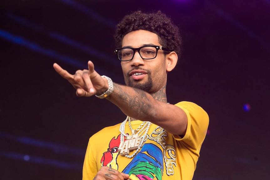 Rapper PnB rock reaches a hand out while holding a microphone in his other hand. 