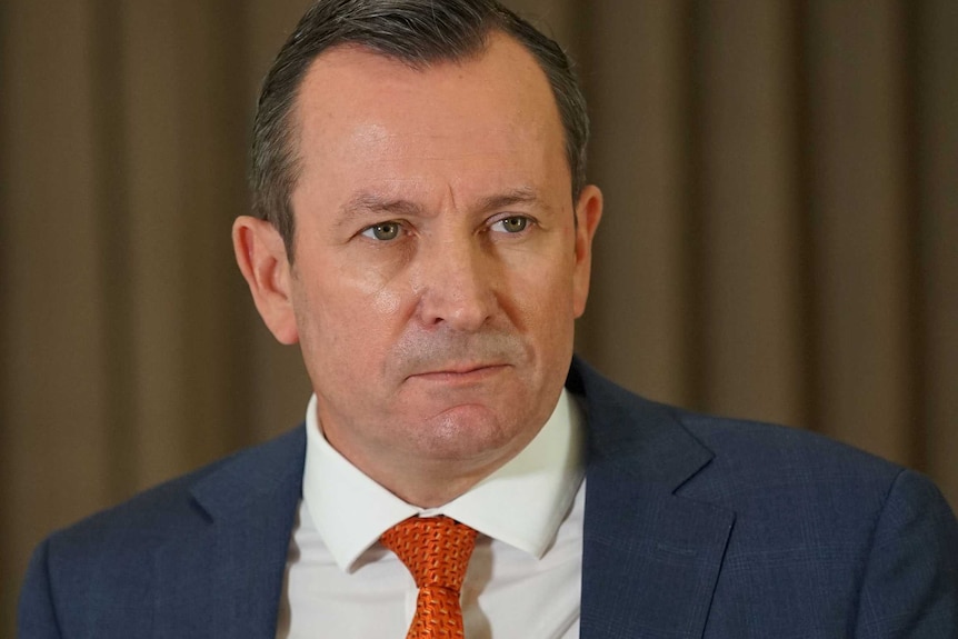 A Mark McGowan at a press conference wearing a blue suit and orange tie.