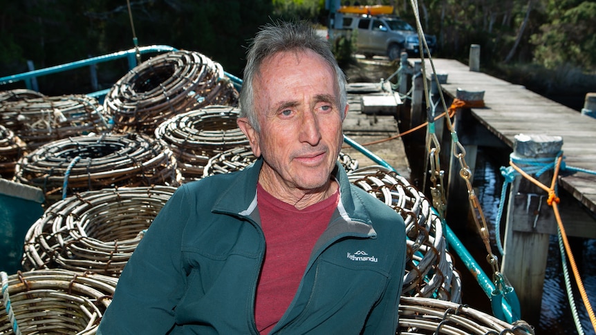 A man stands on deck of crayboat by a jetty, craypots on deck behind.