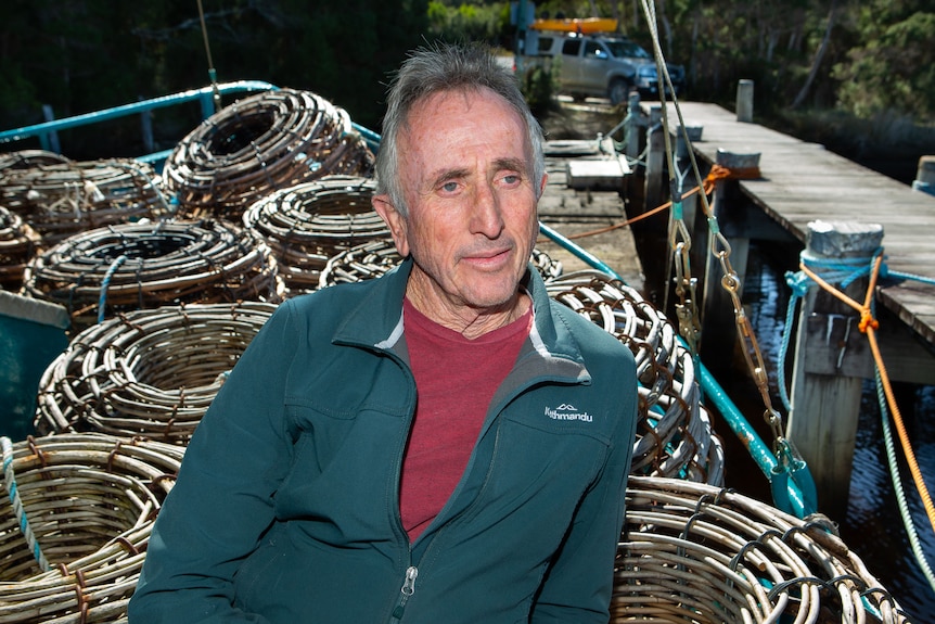 A man stands on deck of crayboat by a jetty, craypots on deck behind.