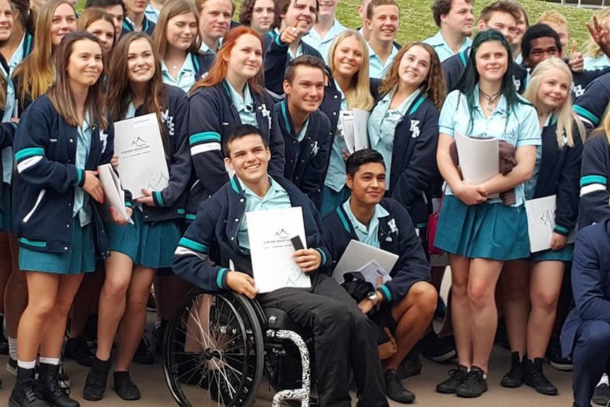 A group of high school students in blue uniform. A male student in a wheelchair is at the front of the group.