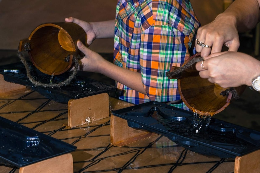 Boy and mother's hands pouring buckets of water into fish-shaped moulds.