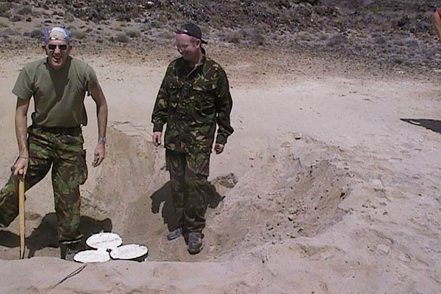 Alan stans with a shovel in hand beside a colleague above a mine that has just dug out