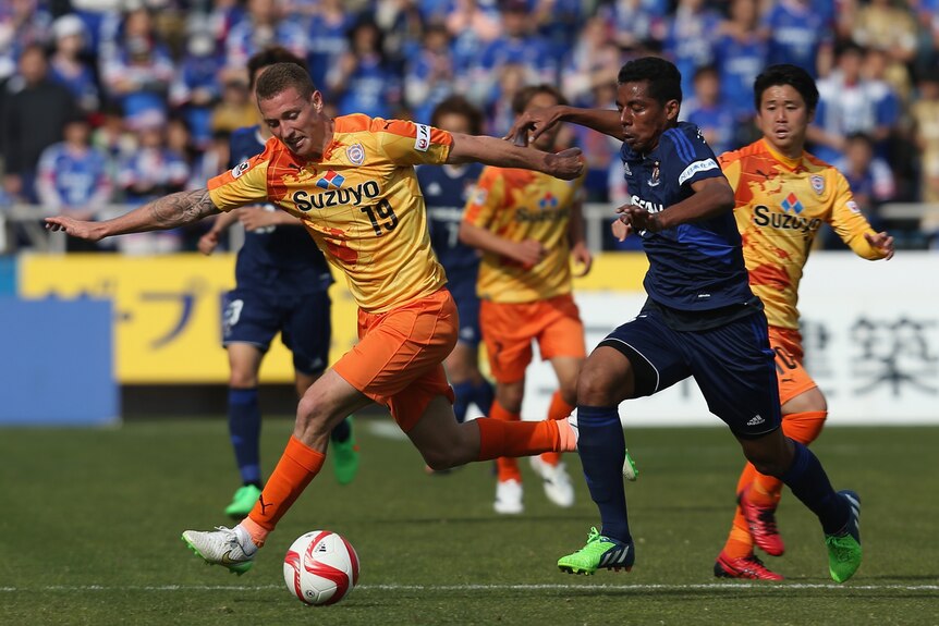 Two male soccer players competing for the ball during a game in Japan