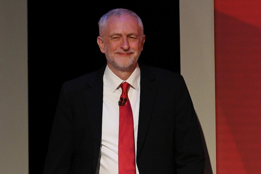 Jeremy Corbyn carries papers in his right hand as he walks into the tv studio wearing a black suit, white shirt and red tie