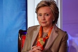Hillary Clinton sits on stage with hands clasped