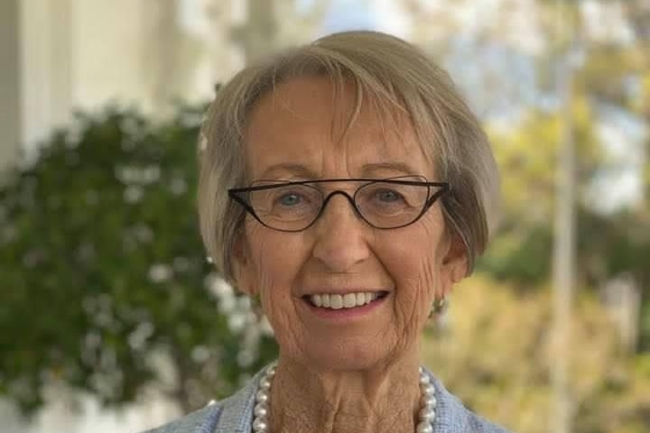 A smiling grey-heared woman wearing glasses