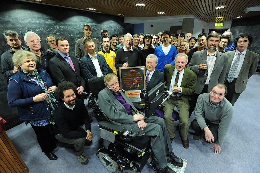 Stephen Hawking is presented a 300-millimetre silicon wafer by a group of people.