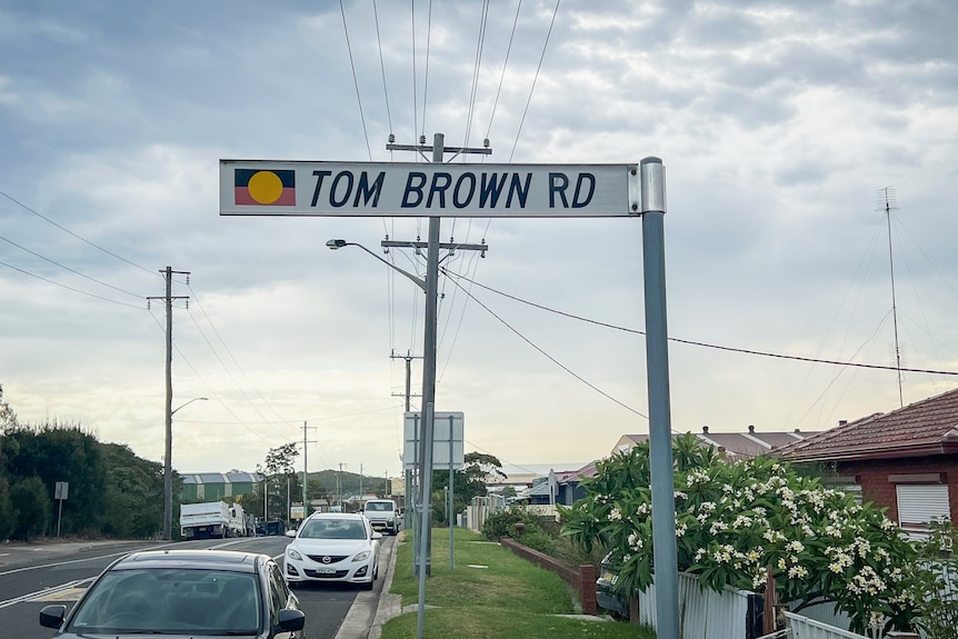 A white street sign with an Aboriginal flag that says 'Tom Brown Rd'