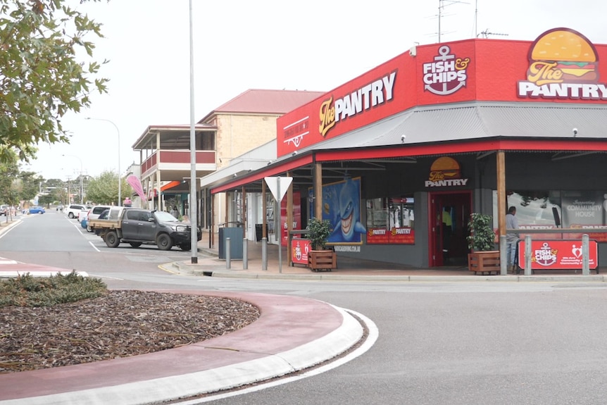 Street scene from across the road of roundabout, trees on left and red verandah shop building