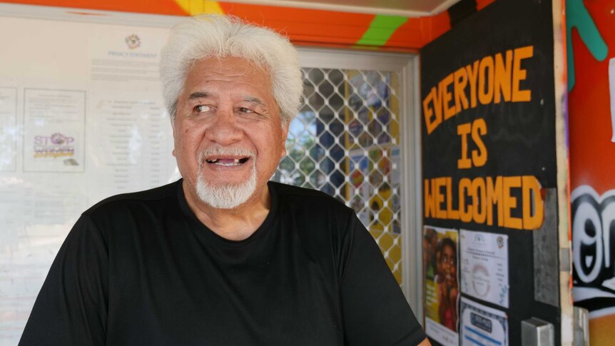 Portrait of Maori man with white hair standing on the porch of an orange building