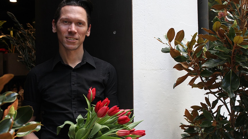 A man in a black shirt holding a bouquet of red tulips.