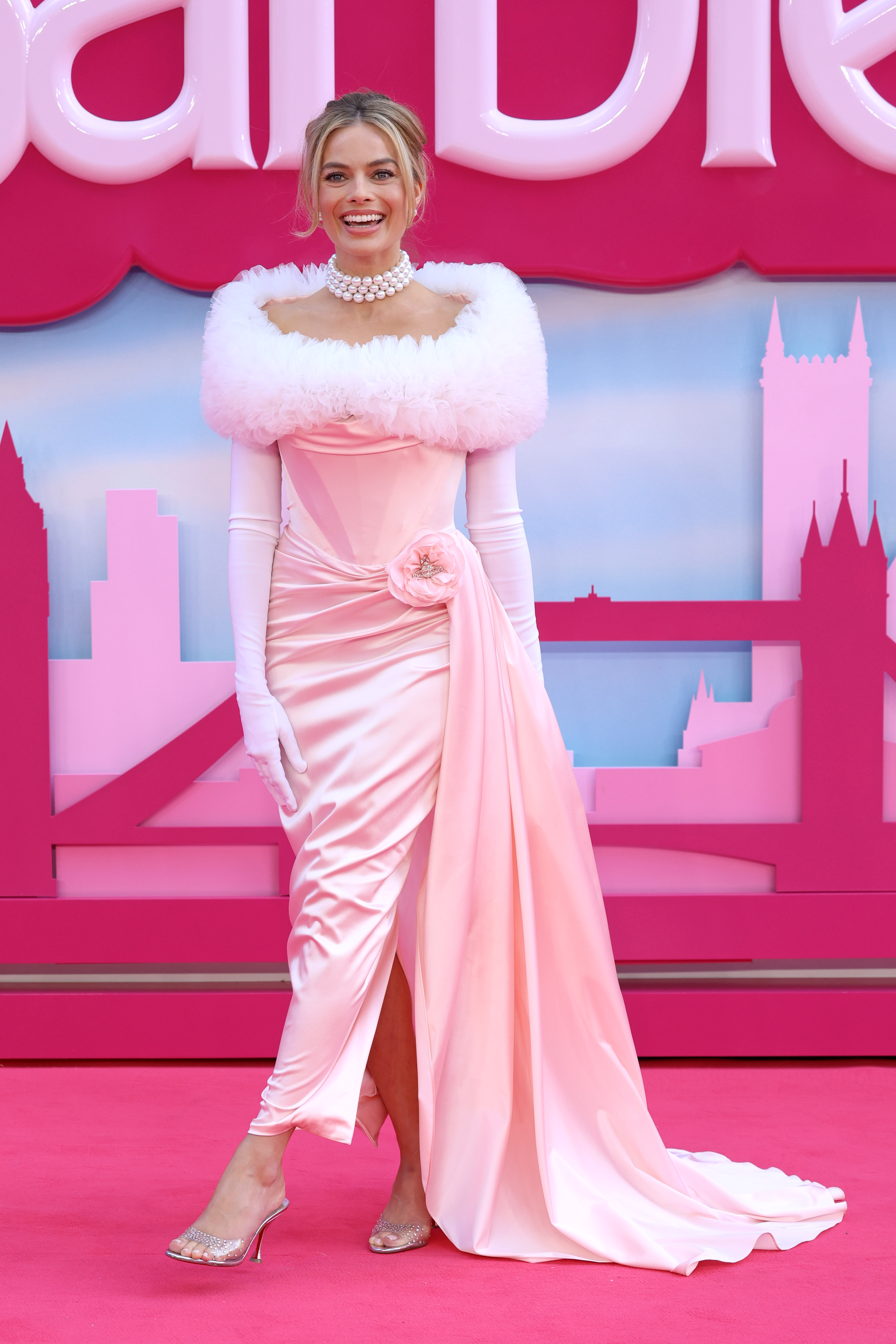 Margot smiles on the red carpet in a pink gown with a fluffy white trim around the shoulders