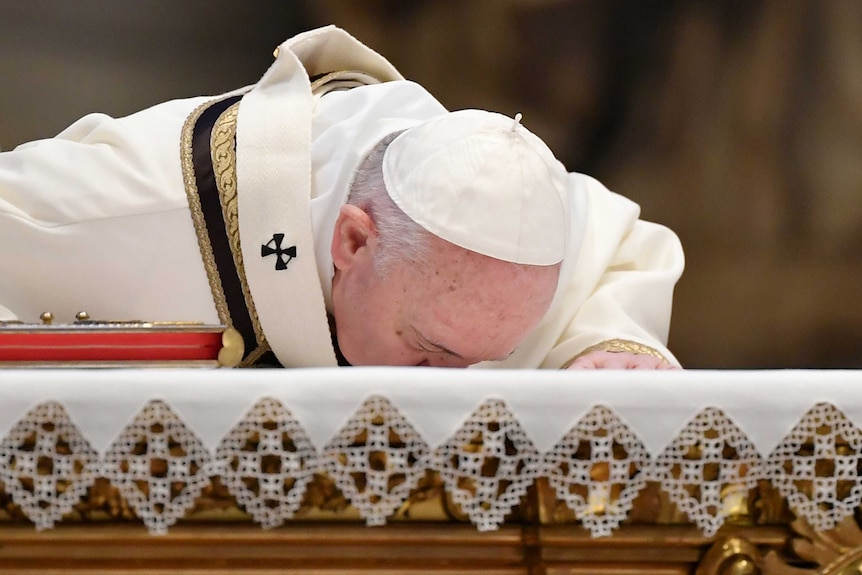 The Pope, wearing a white robe and a zuchetto kisses the altar at St Peter's.