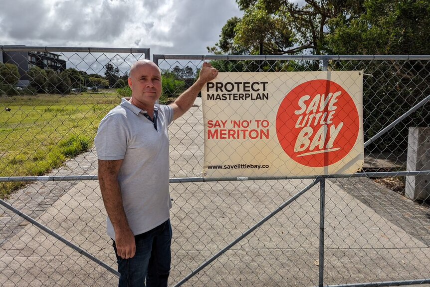 A man standing outside fence with protest sign 'say no to Meriton'