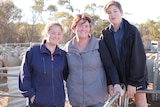 A mother and her two teenage children sit on a fence in a paddock.