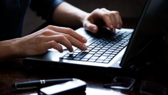 A woman's hands type on a laptop keyboard.