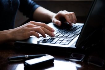 A woman's hands type on a laptop keyboard.