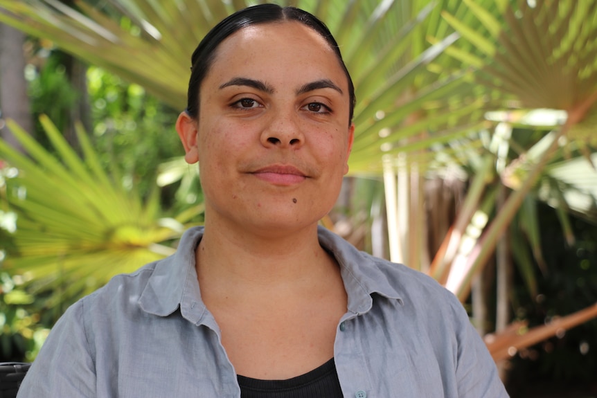 A woman with a grey shirt looks seriously at the camera. Her hair is pulled back.