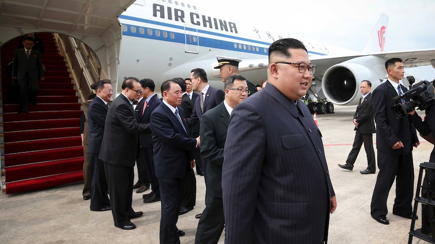Kim Jong-un on tarmac. There is an Air China plane and officials in the background.