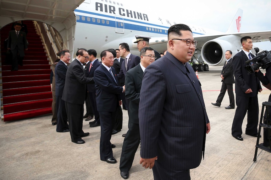 Kim Jong-un on tarmac. There is an Air China plane and officials in the background.