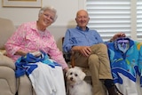 A smiling elderly couple hold up Sydney 2000 volunteer uniforms